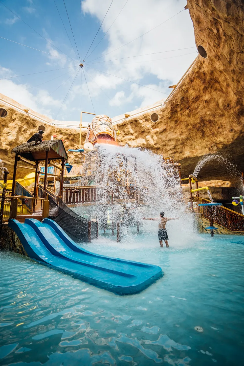 Bezoekers spelen onder een grote waterval in een overdekt waterpark