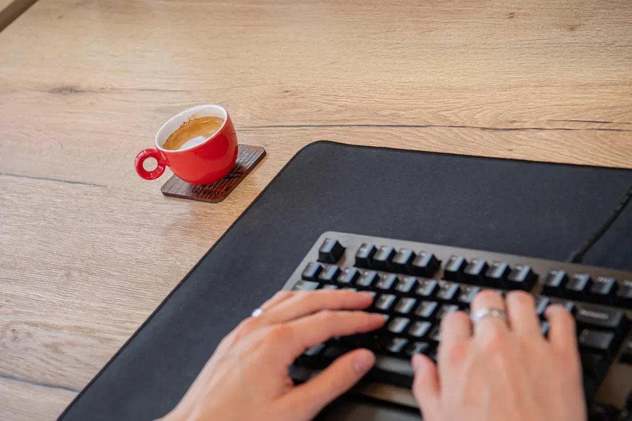 Handen op een toetsenbord aan een bureau, met een kop koffieernaast